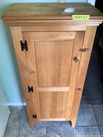 Front view of the wooden cabinet showing single door with black hinges, wooden knob, and some surface stains and scratches.