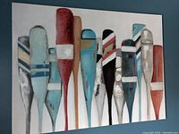 Front view of the canvas wall art showing eleven vertically arranged paddles in various colors and designs on a white background.