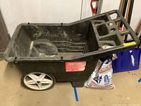Side view of the Craftsman black plastic yard cart showing solid white wheels and storage compartments.