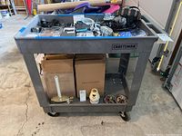 Front view of gray plastic Craftsman hand cart with assorted items on surface and lower shelf.