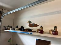 Shelf displaying seven wooden duck decoys and one duck on a stand, showing full group from side angle