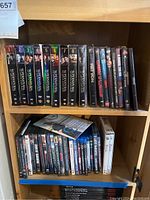 Photo of wooden cabinet shelf holding DVD and Blu-ray cases including complete Supernatural series season sets and other movie titles.