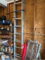 Full view of aluminum extension ladder leaning against wall near shelving in garage, including surrounding items.