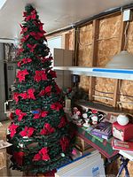 Folding poinsettia Christmas tree with red poinsettias and lights, collapsible design, set up in garage with surrounding items including dolls and candle holders.