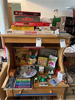 Overview of various toys and games arranged on a wooden shelf including board games, coloring sets, and collectible items.