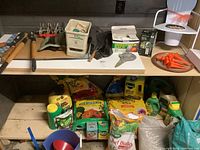 Wooden handled garden tools, gardening gloves, orange stakes, boxes with garden supplies on table surface.