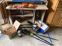 Photo of all items grouped near a small shelf including hiking sticks, Coleman stove and propane canister, Igloo cooler, insect repellent, bug zapper, survival whistle, trail tape, lava rock, heat warmers, and ponchos.