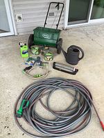 Overview of garden equipment lot showing green Scotts spreader, three hoses including Craftsman, watering can, and garden chemicals.