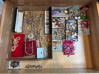 Overview of large assortment of costume jewelry including bracelets, earrings, and necklaces. Items arranged in cardboard trays with varied packaging and loose pieces.