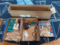 Full view of jewelry contents in open boxes showing necklaces, mood rings, pins, and some earrings
