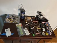 Full view of all items arranged on table including lighters, cutters, lanterns, clock, compasses, and keys.