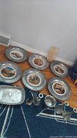 Wide view showing all pewter plates, candle holders, bowl, tray, and tin funnel on floor near wall.