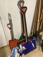 Full view of shovels, rakes, spades and ice melt bags arranged against a wall in a garage showing tool condition and types included.