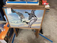 View of four folded snack trays with J MacLeod duck-themed artwork leaning upright, showing full tray tops with flying ducks and wood frames.