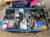Photo of a box containing vehicle chargers, cables, a Wicked HD camera, Motorola P893 phone, phone case, magnifier, headphones and earbuds.