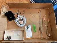 Top-down view of cardboard box containing pin, earrings, necklaces, ring, and broken chain