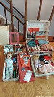 Photo showing two vintage Ginger dolls, various hats, clothes, and a decorative storage case all arranged on a wooden floor with stairs background.