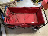 Top-down view of red collapsible wagon showing inside fabric seat and part of metal frame and wheels.