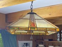Front angle view of Tiffany style stained glass ceiling light hanging from a metal chain showing cream, amber, and green geometric patterned glass panels.