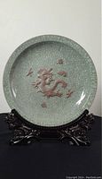 Front view of round celadon glazed ceramic dish with raised brown dragon in center and crackled glaze pattern