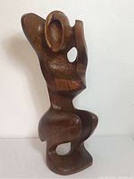 Full view of the wooden sculpture showing the full seated abstract figure, highlighting the form and posture.