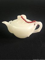 White jade tea pot front angle showing spout, handle, and red beaded string latching lid