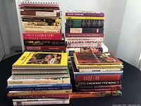 Stack of various cookbooks showing titles such as Keto Cooking, The Silver Plate Cookbook, The New Basics Cookbook, Cook with Jamie, and more.