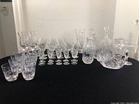 Full lot overview showing all crystal glassware including wine glasses, decanters, and serving dishes arranged on black cloth.