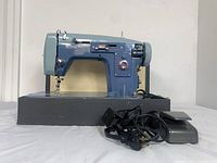 Blue Domestic Sewing Machine Model 762 with attached foot pedal and power cord sitting on black base surface