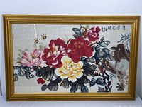 Front view of the framed cross stitch showing peony flowers and a bird in a gold frame