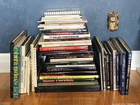 Photo showing large selection of assorted photography books stacked and lined on floor near wall, including titles in color compendium and regional photo collections