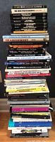 Stack of 30 photography books arranged vertically, showing spines with titles and authors, mostly black and white with various colored spines.