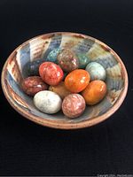 14 polished semi precious stone eggs displayed in pottery dish with brown, blue, rust swirls on beige base