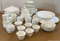 Photo showing full Shinepukur china set arranged on a wooden table, includes various plates, bowls, cups, serving dishes, milk and sugar holders, covered dish and teapot.