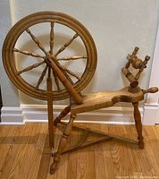 Full view of the vintage wooden spinning wheel showing the large wheel, spindle, and treadle mechanism.