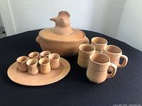 Full view of all terra cotta pottery items on a black tablecloth: large rooster pot, oval dish with small pots inside, and 4 mugs.