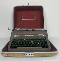 Front view of the Royal Quiet De Luxe typewriter inside its open case with green keys and red lining.