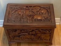 Close-up angled side view of the chest focusing on carved wooden animal motifs and texture.
