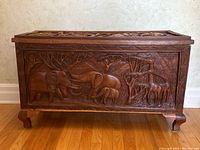 Front view of carved wooden chest showing elephant and giraffe wildlife scene on front panel.
