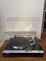 Front view of turntable on wooden surface with dust cover open, cords visible at rear