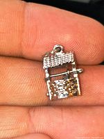 Close-up photo showing the front and details of the small sterling silver wishing well charm being held between fingers.