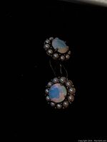 Photo shows the front view of the two round earrings each with a central opalite gem surrounded by faux pearls set in silver plated frames.