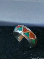Close-up photo of a chunky silver ring featuring blue stone and red coral inlays in an angular geometric pattern.