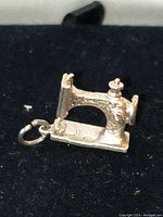 Front and side view of chunky .925 sterling silver vintage Singer sewing machine charm on black background