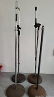 Four microphone stands of varying heights with round weighted bases. Some rust visible on bases and poles.