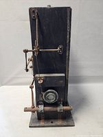 Front view of antique wooden camera or projector showing lens and attached metal components.