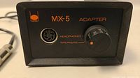 Front view showing the headphone/speaker port, volume knob, and MX-5 branding on adapter