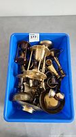 Blue plastic bin containing various brass items with several candlestick holders and bowls.