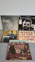 Five Beatles-related vinyl LPs, including Sgt. Pepper's Lonely Hearts Club Band, Imagine, RAM, Wings At the Speed of Sound, and Ringo Starr Rotogravure, arranged side by side on a surface.