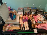 Overview of all 16 dolls laid out on table with a white plastic case behind
